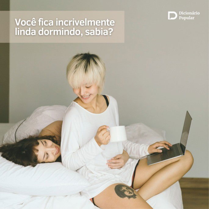 Mulher deitada na cama olha para outra mulher sentada com o laptop no colo