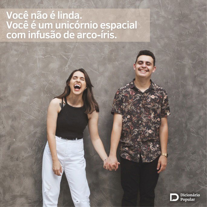 Casal de pé, em frente a uma parede cinza, rindo bastante