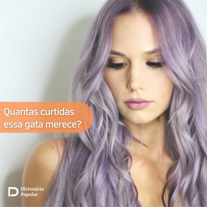 Mulher de cabelos longos e roxos posa para a foto olhando para baixo em frente a uma parede branca