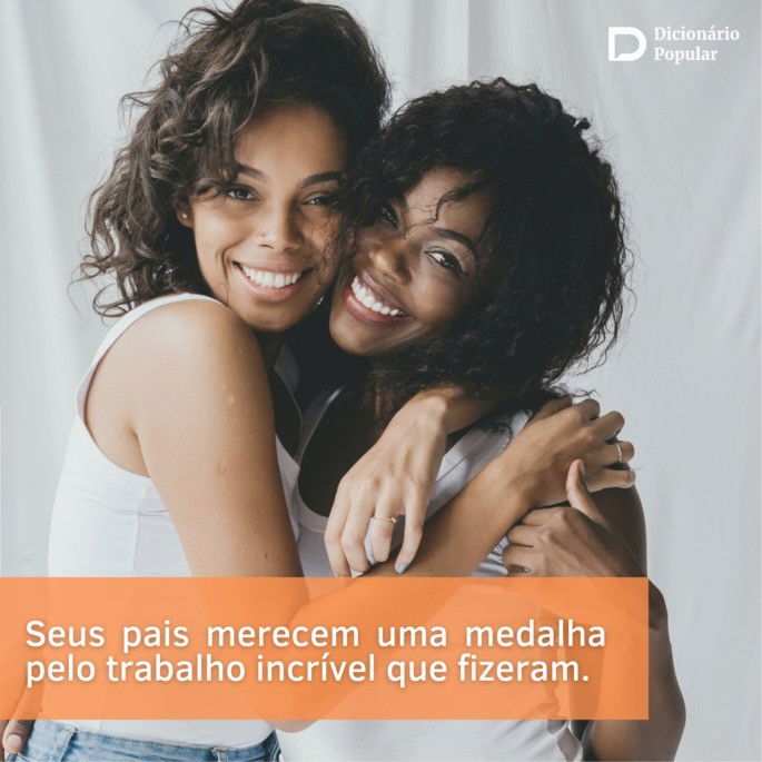 Duas mulheres de camisa branca, uma pé e outra sentada, se abraçam em frente a uma cortina também branca