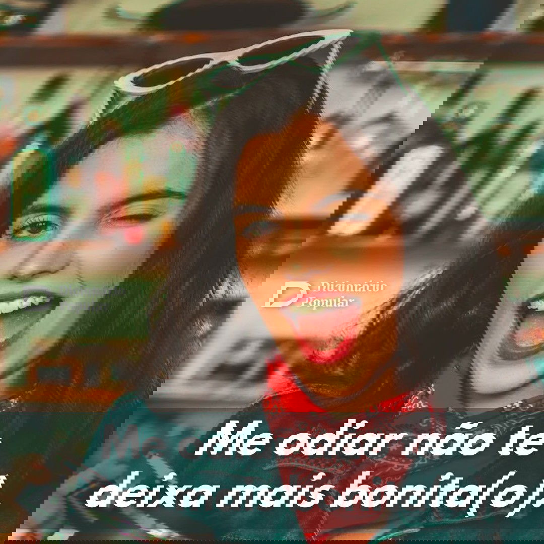 Mulher de batom vermelho e óculos escuros na cabeça pisca para a câmera com um sorriso de boca aberta