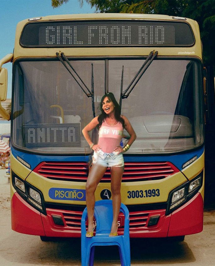 Gretchen em pé em uma cadeira de plástico azul em frente a um ônibus