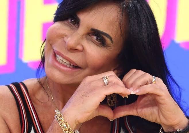 Gretchen sorri e olha para a cãmera fazendo um coração juntando as mãos