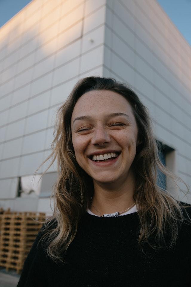 Menina de casaco preto sorri de olhos fechados
