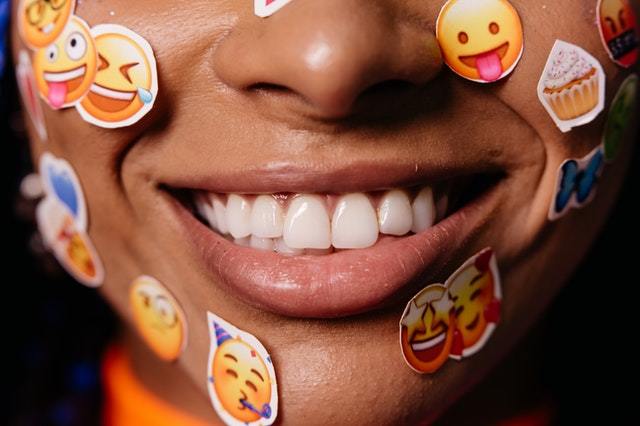 Sorriso aberto com adesivos de emoji colados ao redor da boca