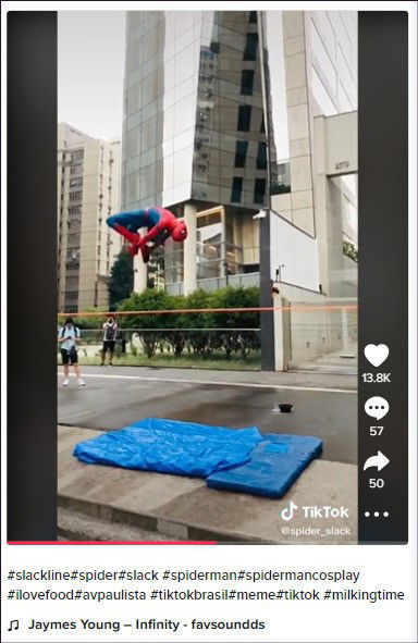 Homem vestido de homem aranah faz acrobacias em slackline em local cercado de prédios